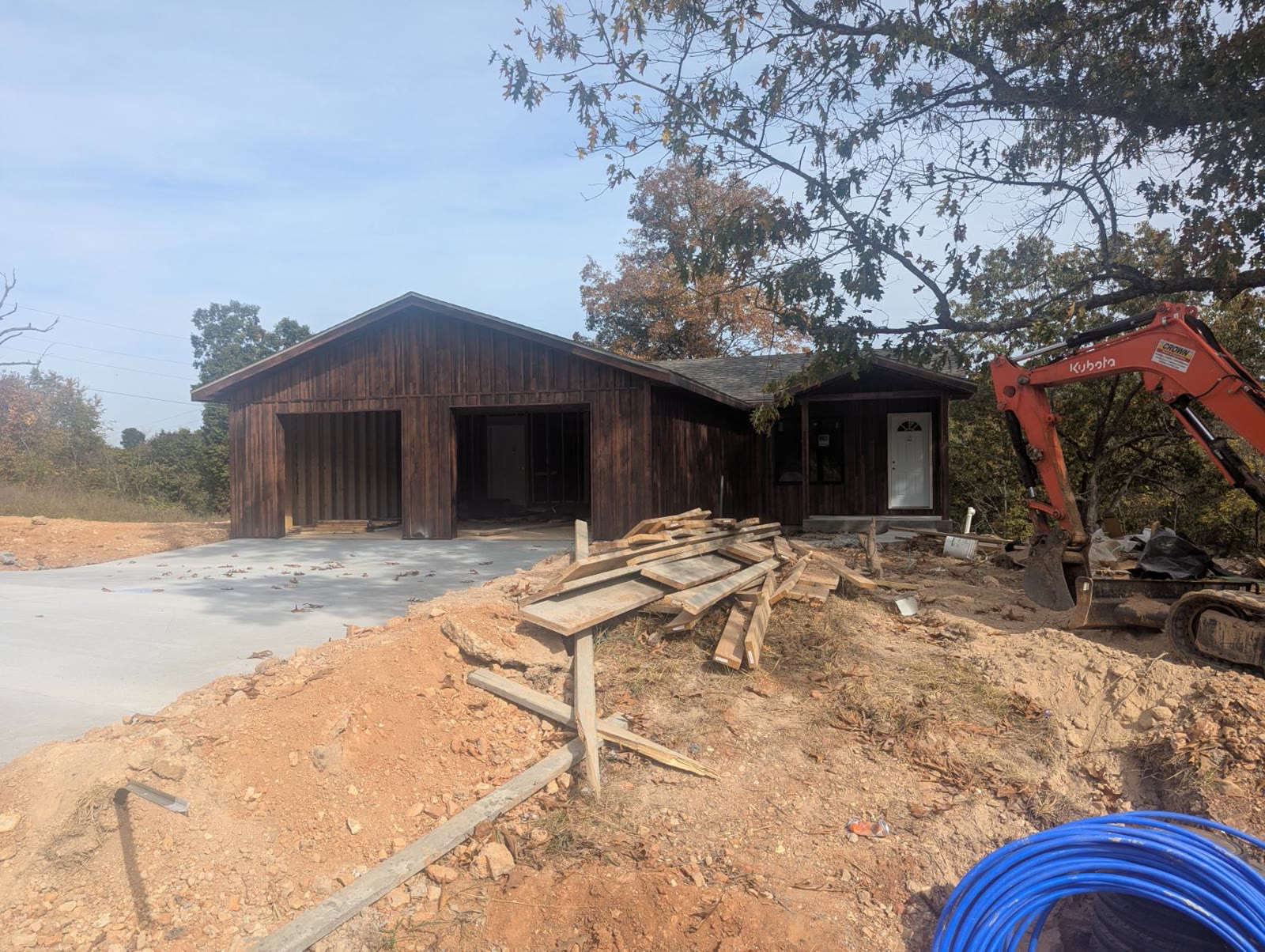 Front of the house, garage bays open, siding on, excavator at the side